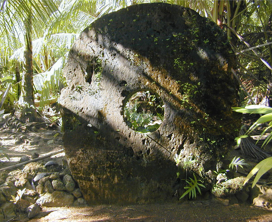 A large rai stone disc with a central hole, set on a stone base in the Yap forest.