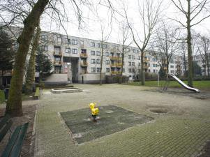 Paved inner courtyard between housing blocks with a small sandpit and bare trees in winter.