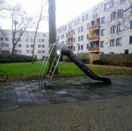 Metal slide on a paved courtyard in front of a housing block, no greenery around it.