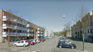 Wide brick street in Venserpolder lined with parked cars and four-storey housing blocks, few trees.